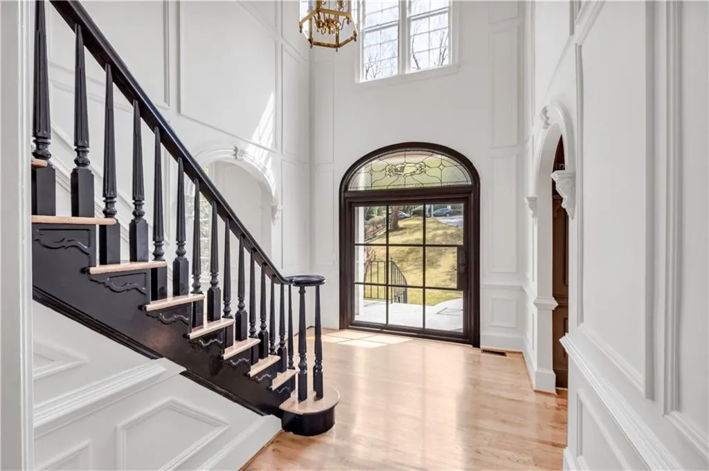 Foyer featuring a decorative wall, light wood-style flooring, stairway, a chandelier, and a towering ceiling