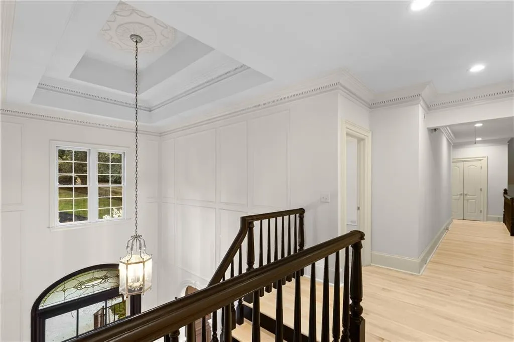 Hallway featuring an upstairs landing, a chandelier, crown molding, light wood-style floors, and a tray ceiling