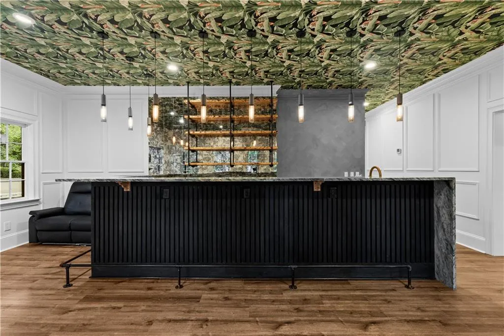 Indoor wet bar featuring a decorative wall, decorative light fixtures, light wood-style floors, white cabinets, and ornamental molding