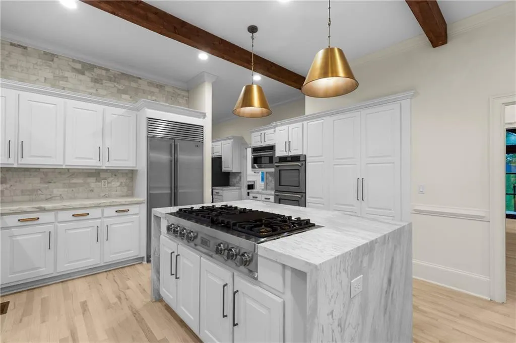 Kitchen featuring tasteful backsplash, light stone counters, a kitchen island, crown molding, and light wood-style floors