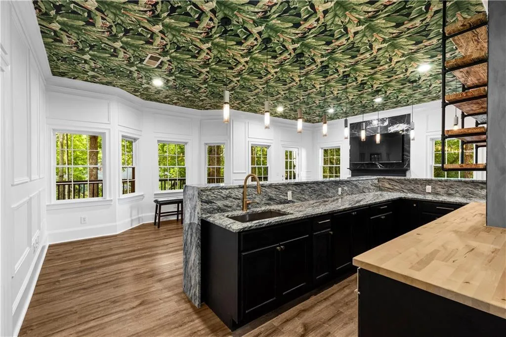 Kitchen with dark cabinets, light stone countertops, pendant lighting, dark wood finished floors, and a decorative wall