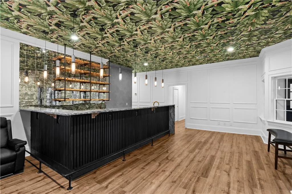 Indoor wet bar featuring a decorative wall, light wood-style floors, open shelves, decorative light fixtures, and dark stone countertops