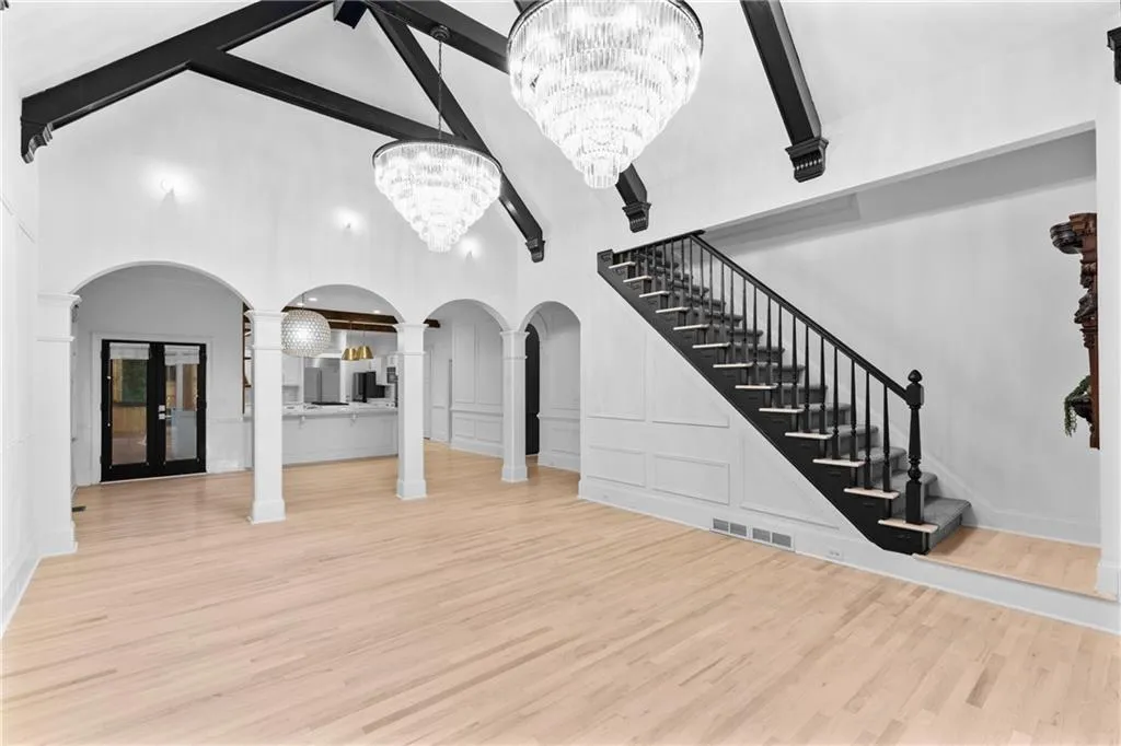 Unfurnished living room featuring beamed ceiling, light wood-type flooring, high vaulted ceiling, decorative columns, and arched walkways