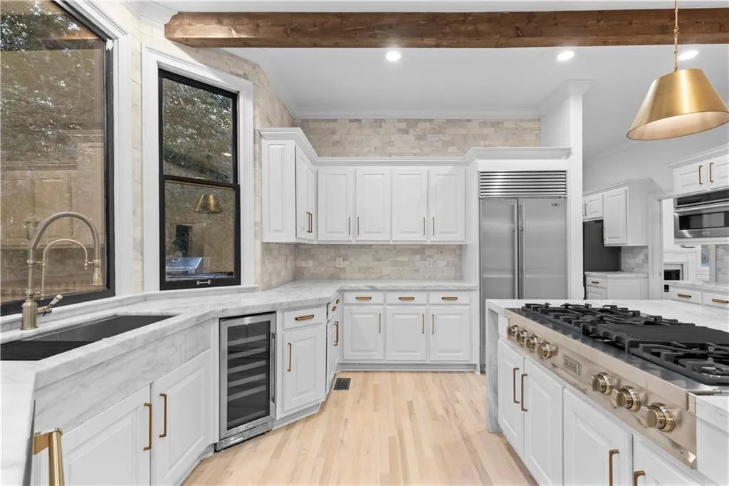 Kitchen with crown molding, appliances with stainless steel finishes, white cabinetry, wine cooler, and light stone countertops