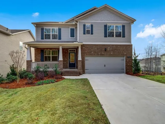 Two-story residence featuring a brick and siding facade, covered front porch with white railing, blue decorative shutters, an attached garage, and a concrete driveway