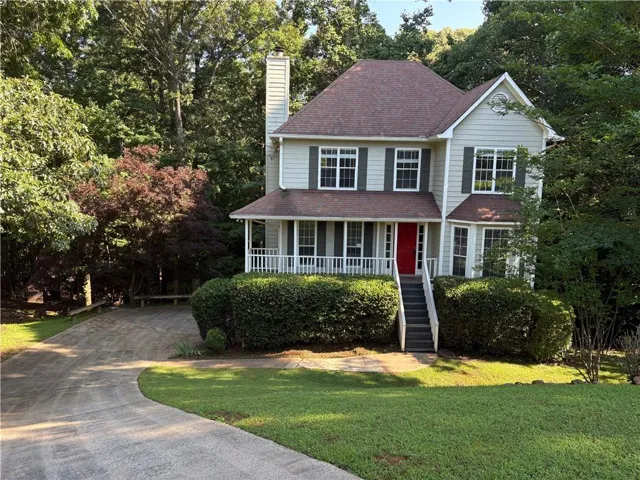 Traditional-style home featuring a prominent red entry door, a covered front porch with white railing, and a bay window