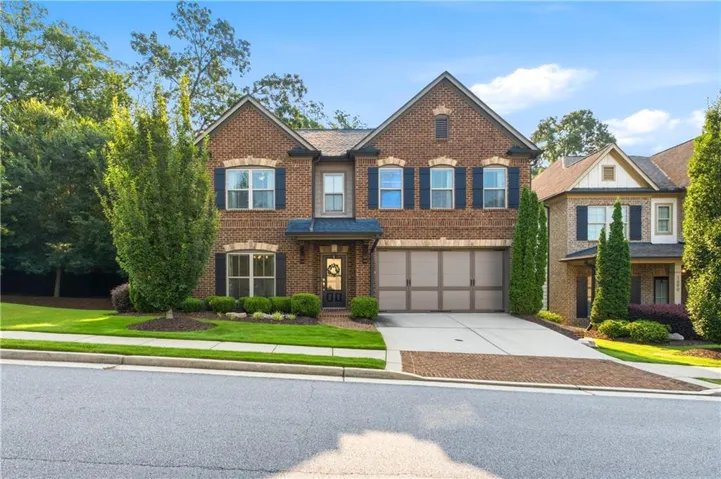 Brick exterior residence featuring a two-car garage, manicured lawn, and mature trees
