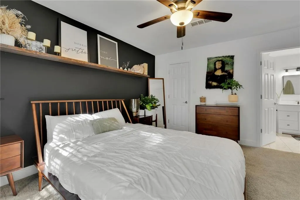 Bedroom with light carpet, ensuite bathroom, and ceiling fan