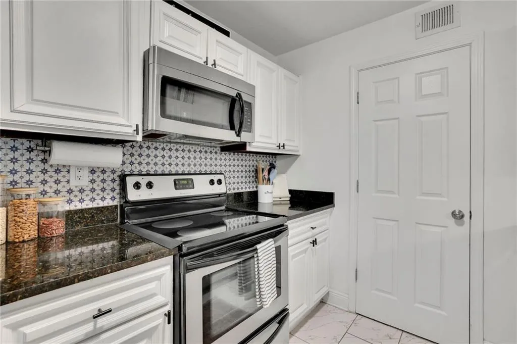 Kitchen featuring decorative backsplash, white cabinetry, stainless steel appliances, and dark stone counters