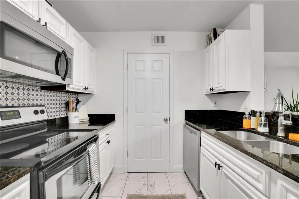 Kitchen with decorative backsplash, white cabinets, dark stone counters, sink, and stainless steel appliances