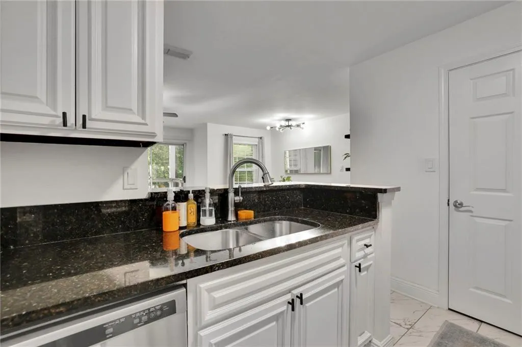 Kitchen featuring sink, dark stone countertops, dishwasher, and white cabinets