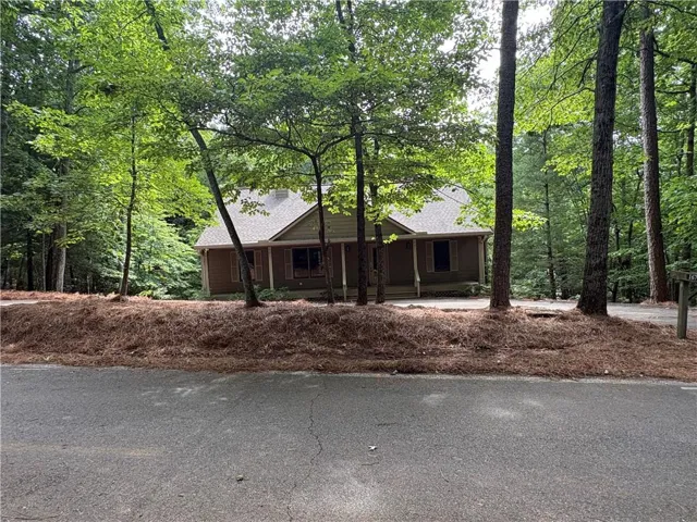 Wooded lot featuring a brown siding exterior, light-colored roofing, and a front porch area