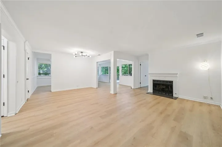 Open-concept living space featuring light wood-finish flooring, a white mantel fireplace with a black hearth, multiple windows, and recessed lighting