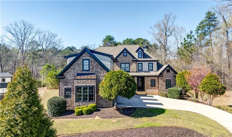 View of front of house featuring stone siding, a standing seam roof, concrete driveway, and a front lawn