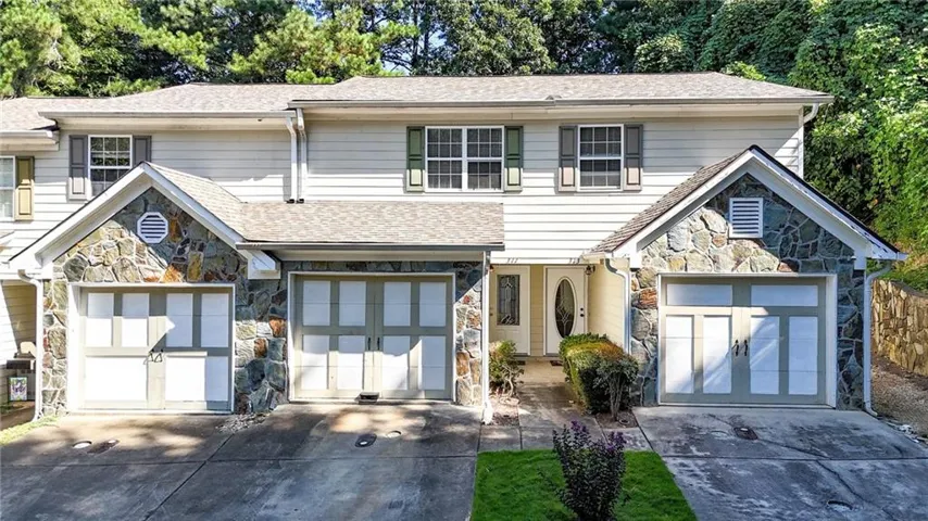 Stone facade accents, dual garage bays, green window shutters, white siding, and a gabled roofline