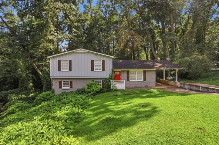 Split-level residence featuring a gray and white exterior, brown window shutters, an attached carport, and a prominent red entry door