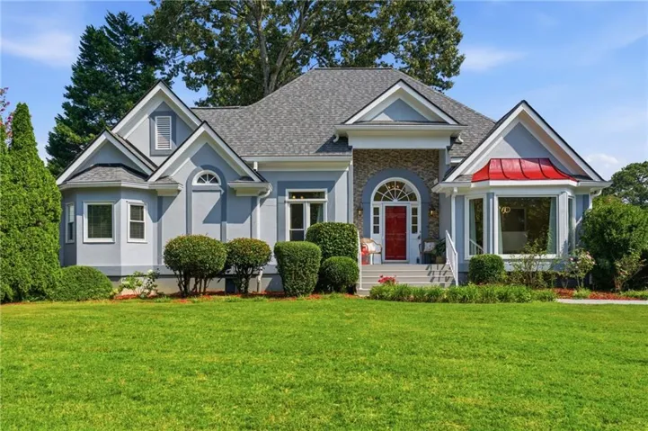 Stucco exterior with stone accents, architectural shingle roof, arched entryway with a red door, bay window with a red metal roof, and a manicured lawn