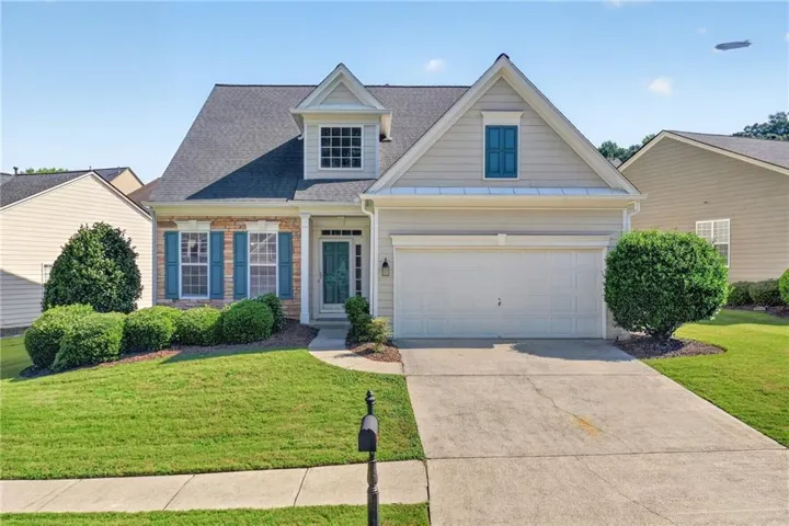 Traditional-style home featuring a gabled roofline, stone and siding exterior, blue window shutters, attached two-car garage, and a concrete driveway