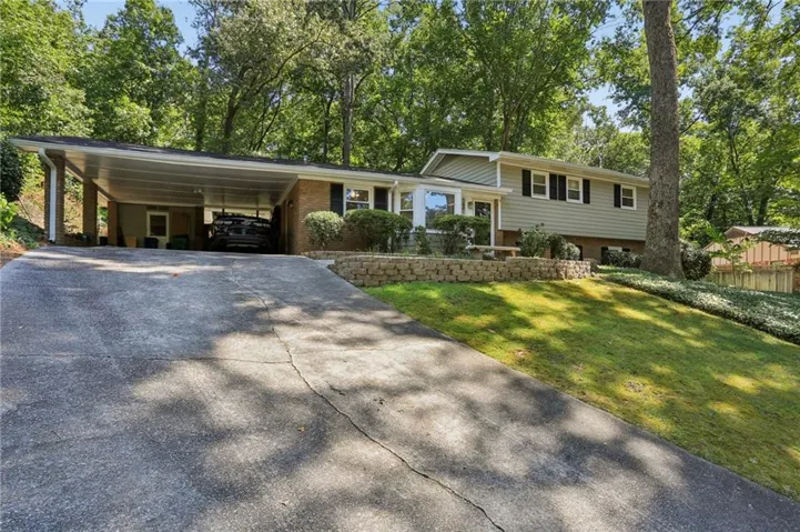 Split-level residence featuring a carport, brick and siding exterior, front landscaping with a stone retaining wall, and a sloped lawn