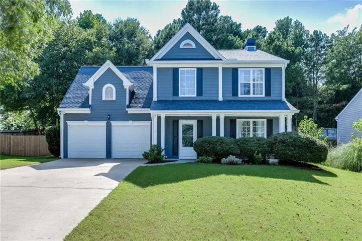 Two-story residence featuring a two-car garage, front porch with white columns, blue siding, and contrasting dark shutters