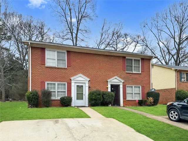 Brick exterior with red shutters, two white entry doors with portico-style surrounds, and a green lawn