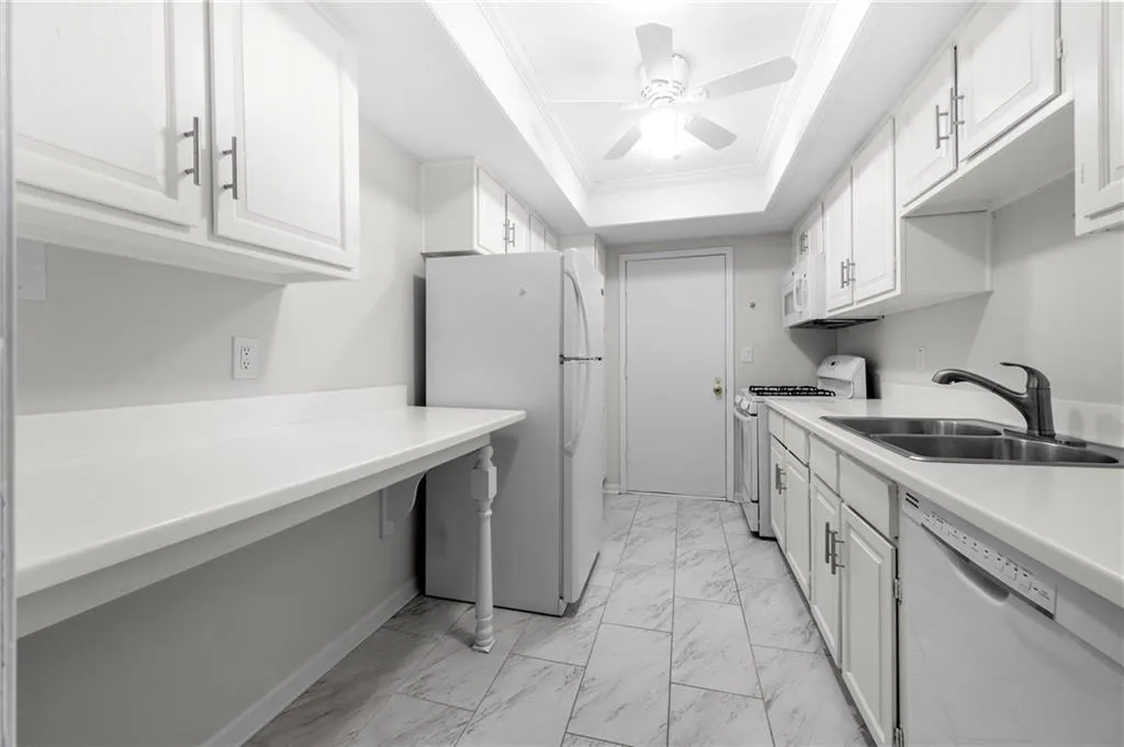Kitchen featuring white cabinets, white appliances, a raised ceiling, and sink