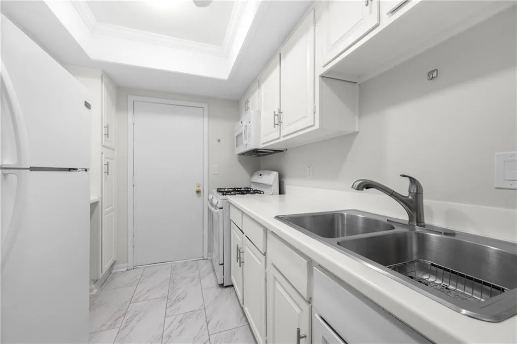 Kitchen with white appliances, white cabinets, crown molding, sink, and a tray ceiling
