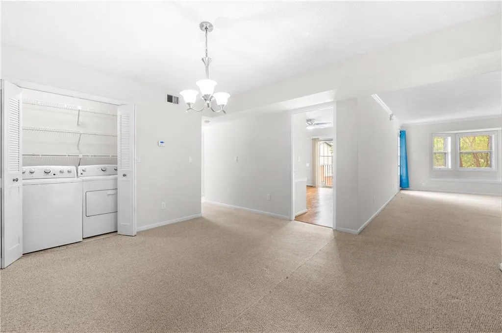 Carpeted empty room featuring ceiling fan with notable chandelier, independent washer and dryer, and a wealth of natural light