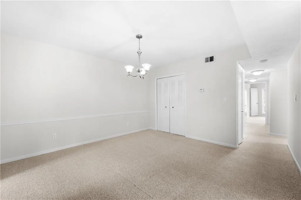 Spare room featuring light colored carpet and a notable chandelier