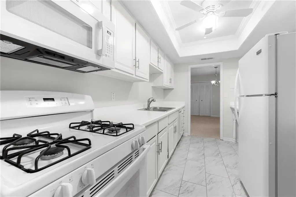 Kitchen featuring ornamental molding, white appliances, a tray ceiling, sink, and white cabinets