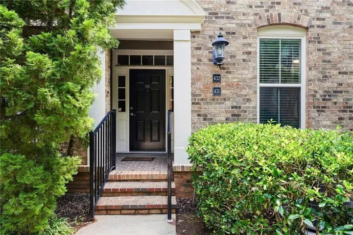Brick exterior with a covered entry, dark paneled door, decorative wall lantern, and foundation plantings
