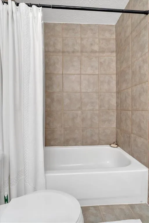 Bathroom with tile patterned floors, shower / bath combo, and toilet. Plenty of storage.