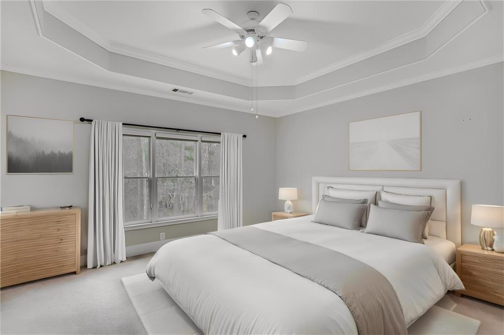 Carpeted bedroom featuring a raised ceiling, ornamental molding, and ceiling fan