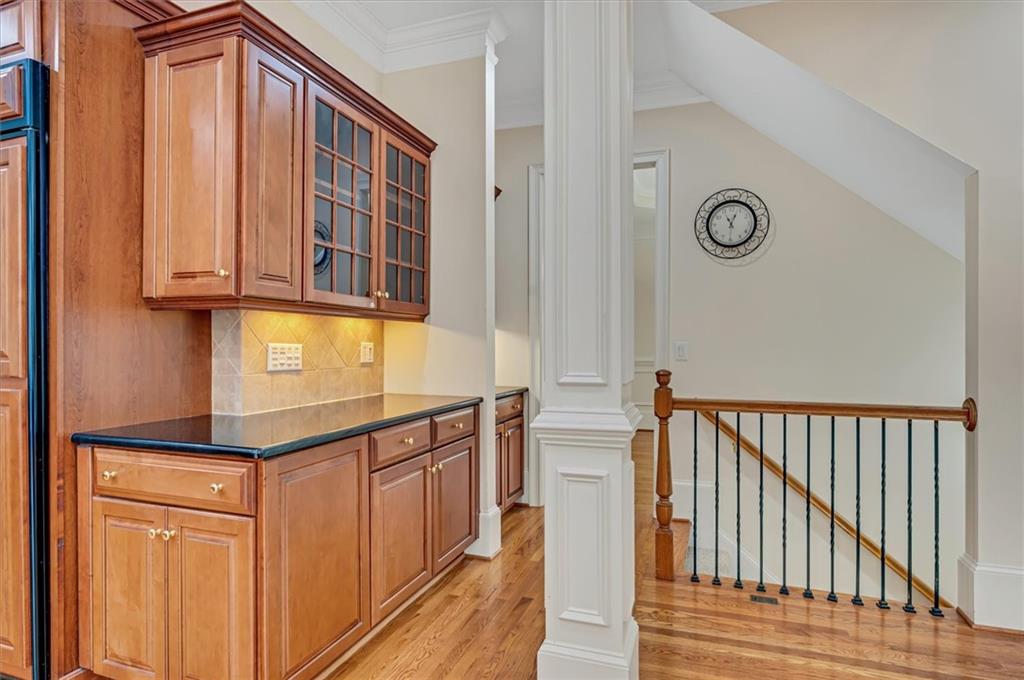 Kitchen with decorative columns, dark stone counters, backsplash, light hardwood / wood-style floors, and crown molding