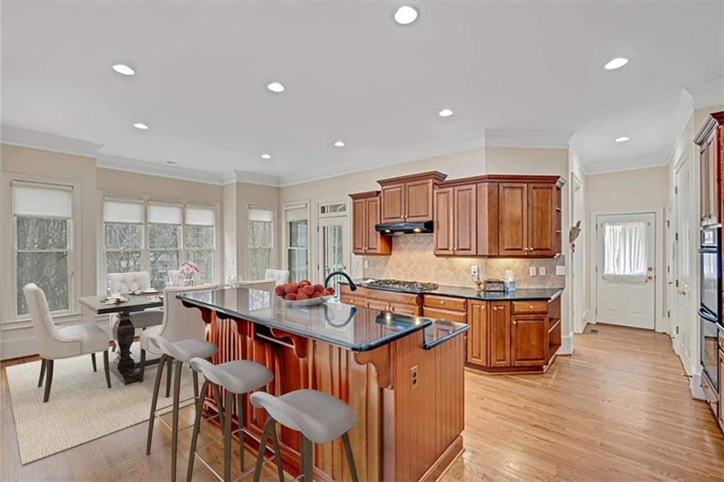 Kitchen featuring crown molding, a kitchen island with sink, light wood-type flooring, backsplash, and a breakfast bar