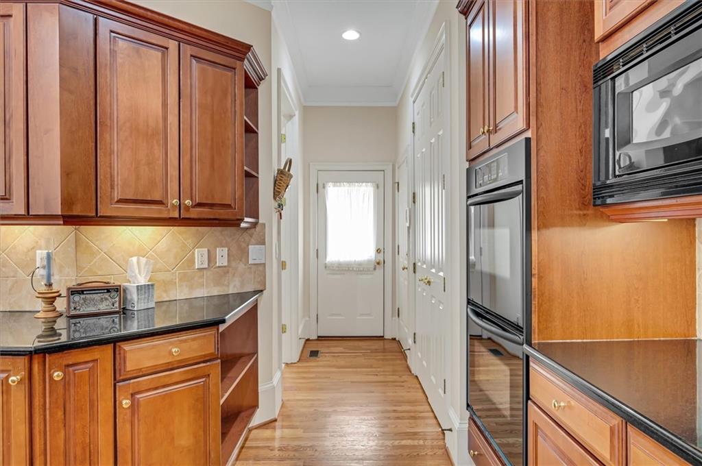 Kitchen featuring built in microwave, light wood-type flooring, tasteful backsplash, double oven, and dark stone countertops