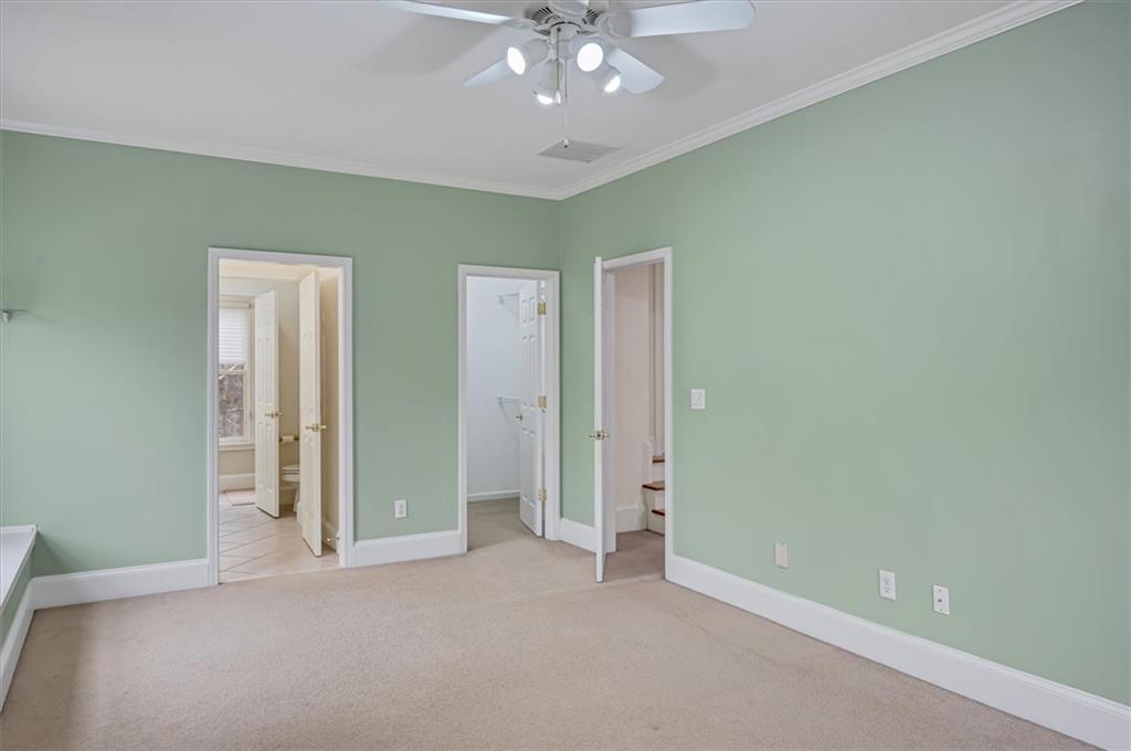 Unfurnished bedroom featuring ensuite bath, ornamental molding, ceiling fan, and light colored carpet