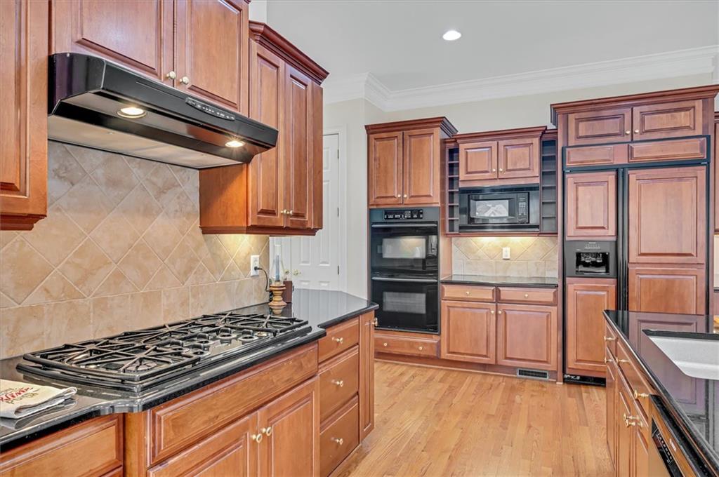 Kitchen with light wood-type flooring, black appliances, crown molding, and backsplash
