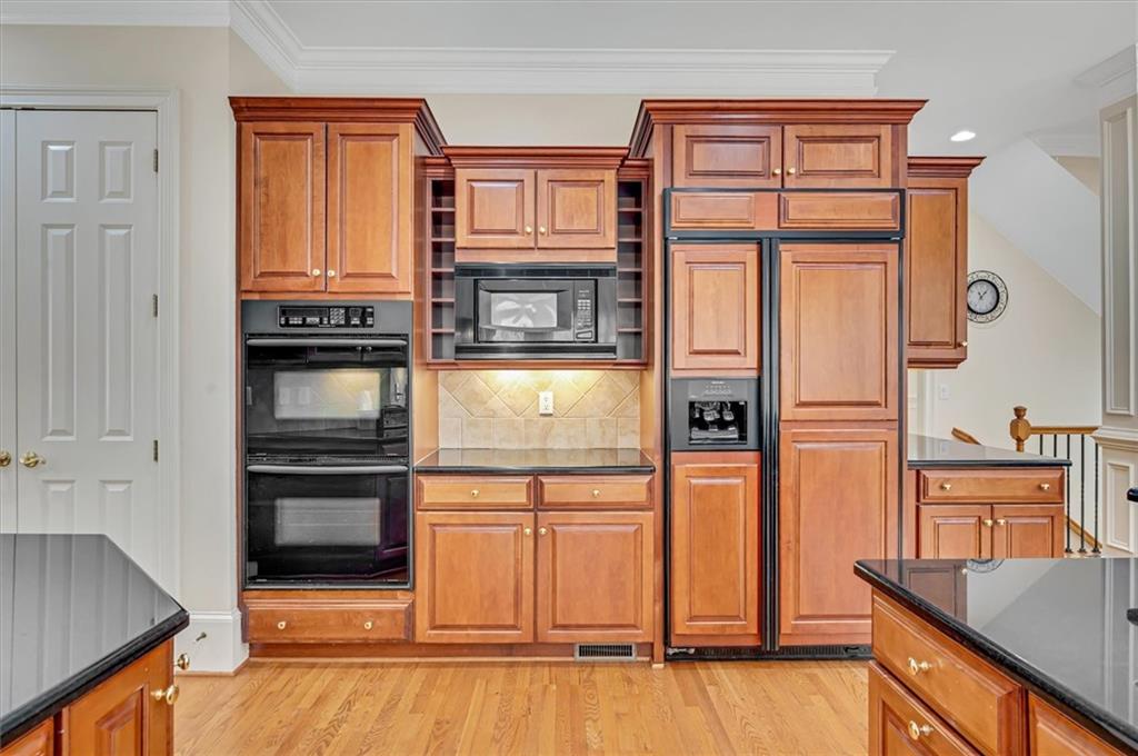 Kitchen with black appliances, light wood-type flooring, crown molding, tasteful backsplash, and dark stone countertops