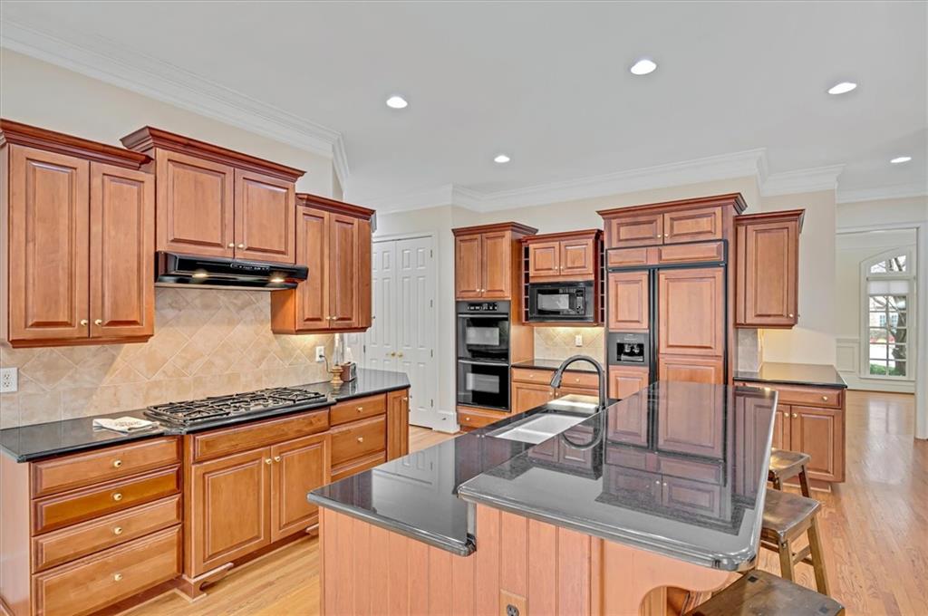 Kitchen with light hardwood / wood-style floors, black appliances, sink, a breakfast bar, and an island with sink