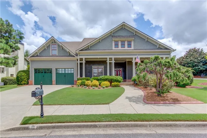 Gable roof design, columned front porch, dual green garage doors, concrete driveway, and a manicured lawn