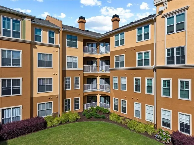 Multi-story stucco exterior featuring multiple windows, private balconies with metal railings, and a manicured lawn with varied shrubbery