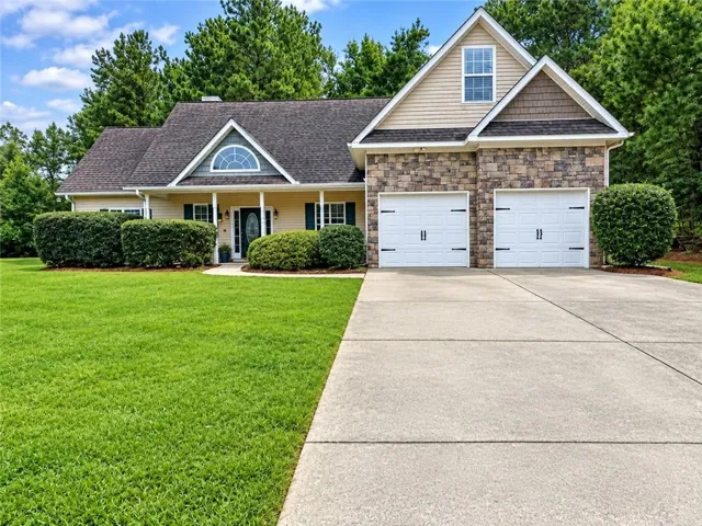 Stone facade detailing, arched window feature, covered front entry, attached two-car garage, and concrete driveway