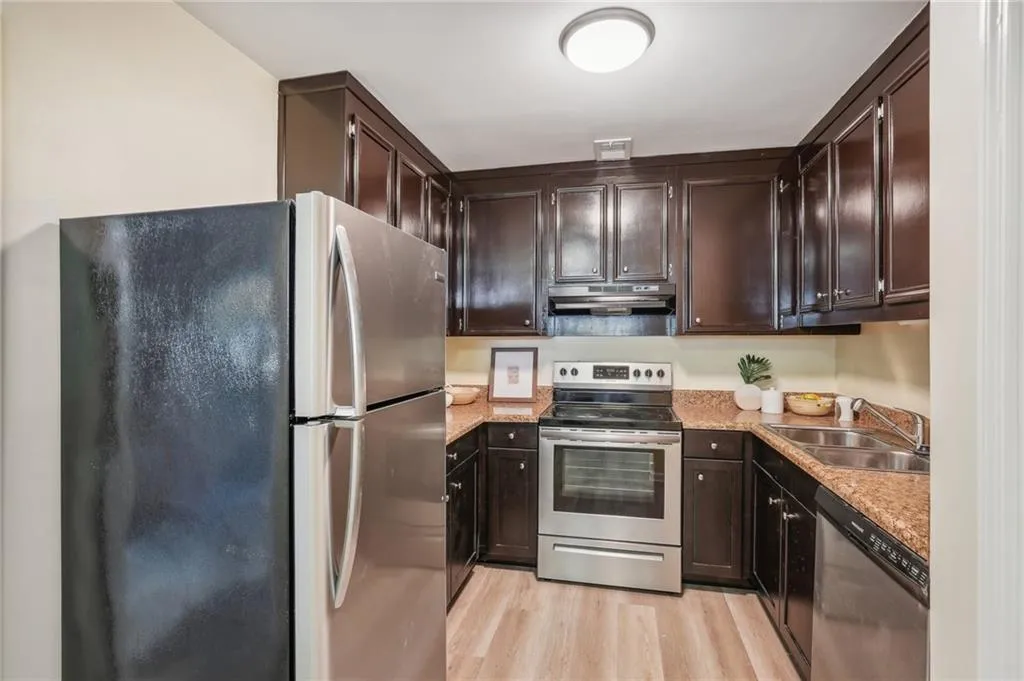 Kitchen with stainless steel appliances, sink, dark brown cabinets, and light hardwood / wood-style floors