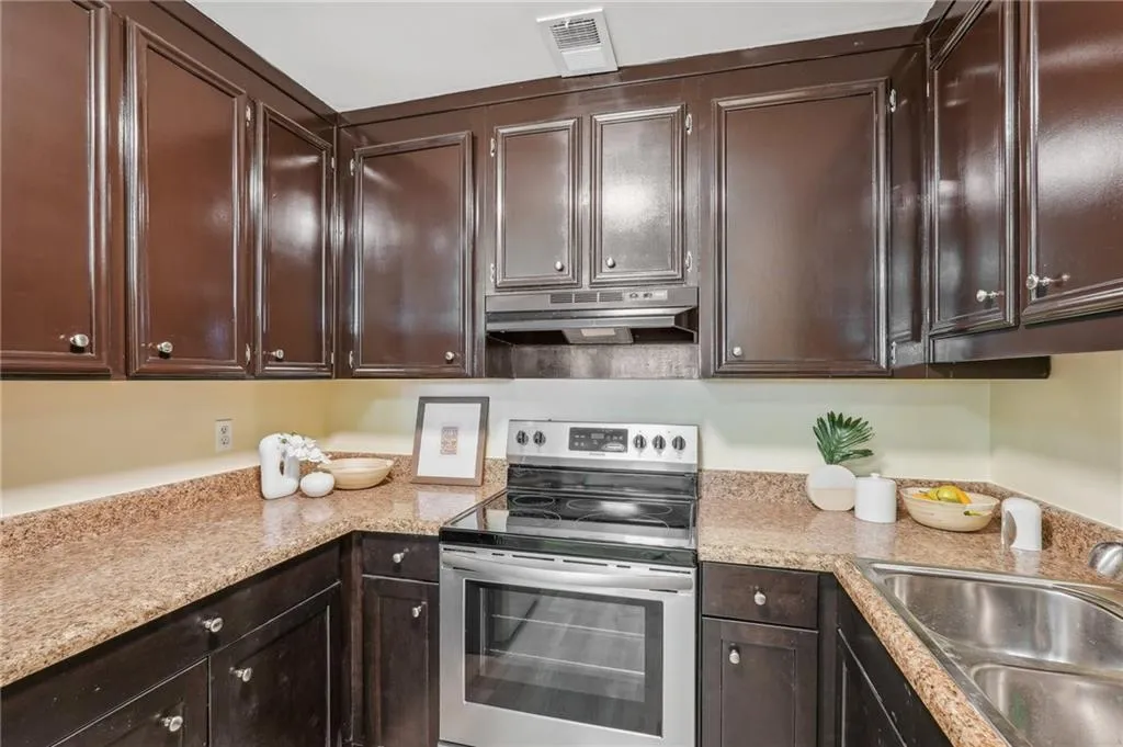 Kitchen featuring light stone counters, sink, dark brown cabinets, and electric stove