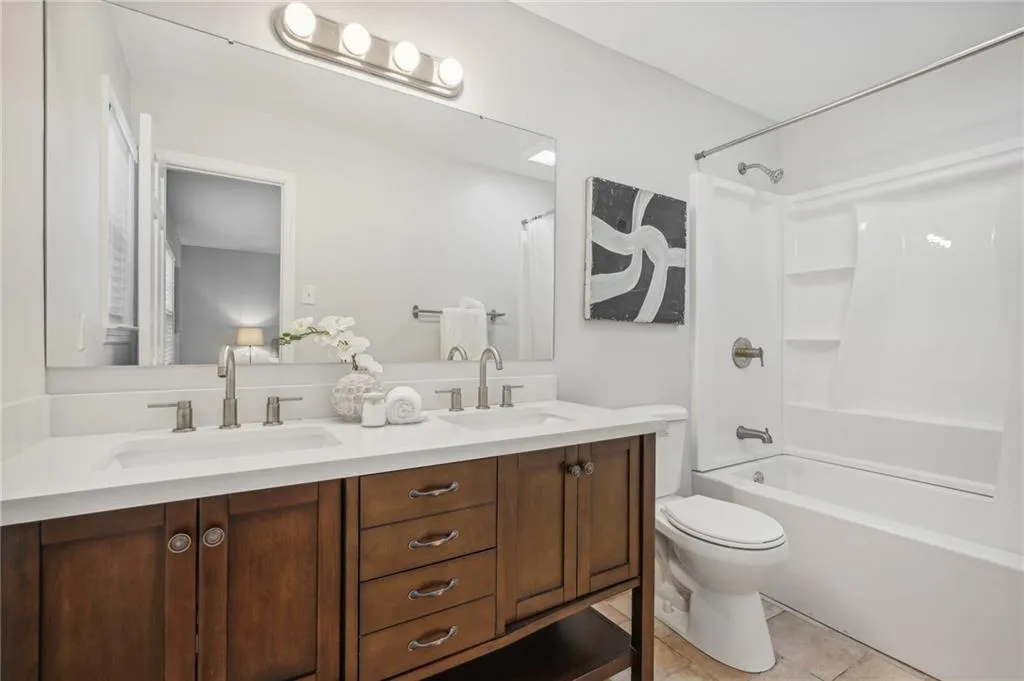 Full bathroom with tile flooring, double sink, tub / shower combination, vanity with extensive cabinet space, and toilet