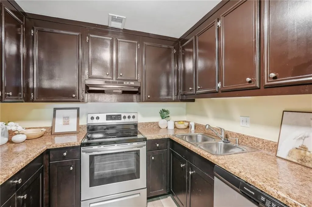 Kitchen with appliances with stainless steel finishes, light stone counters, sink, and dark brown cabinetry