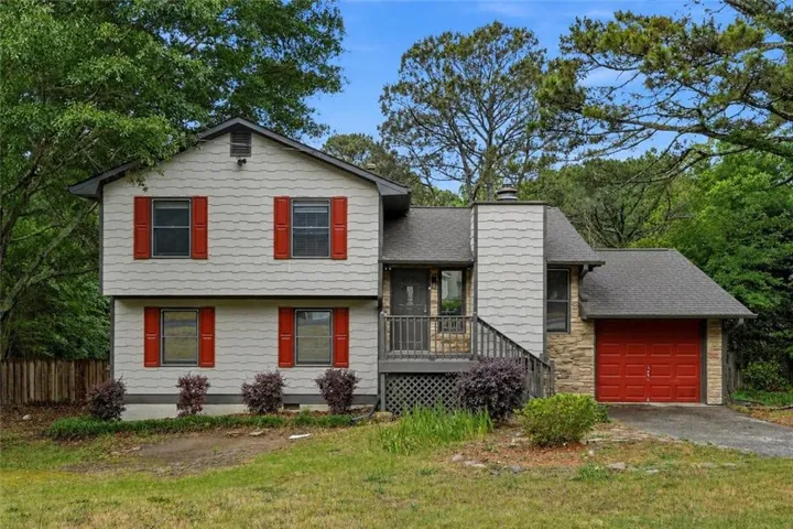 Two-story exterior with shake siding, decorative red shutters, an attached garage with a red door, and stone accents
