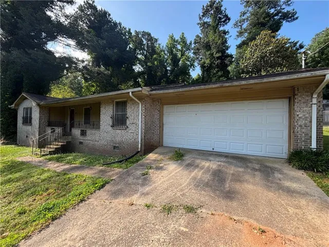 Brick exterior, attached garage, concrete driveway, front porch with metal railings, and mature trees