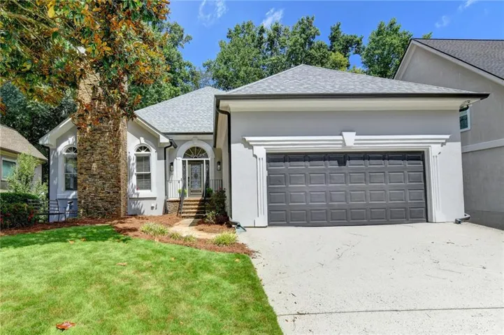 Stucco exterior with a stone chimney accent, arched entryways, a gray asphalt shingle roof, and a two-car garage